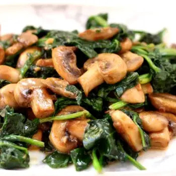 Fresh spinach leaves, sliced mushrooms, and whole almonds displayed together in a bowl