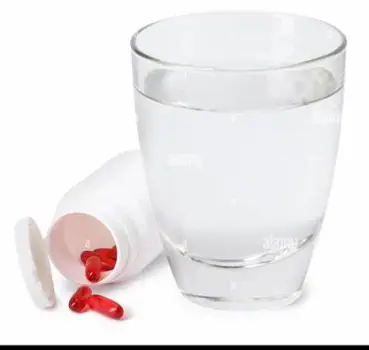 White amoxicillin capsules scattered on a table beside a clear glass of water