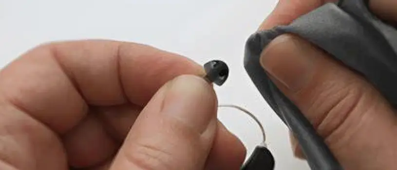 Close-up of hands cleaning an earbud or hearing aid with a soft cloth and mild solution