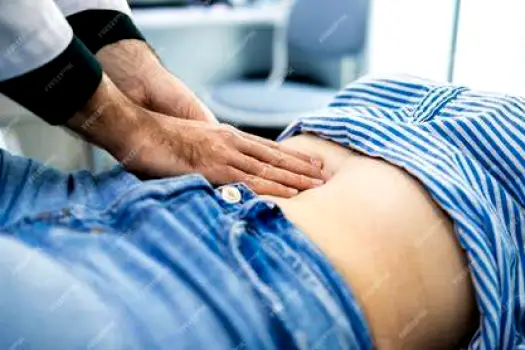 Doctor examining a patient standing, asking them to cough while palpating the abdomen to locate pain and assess for hernia or other issues