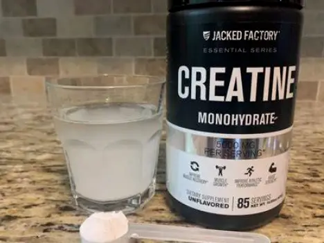 Close-up of a measuring scoop filled with creatine monohydrate powder beside a glass of water
