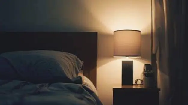 A calm, dimly lit bedroom with a neatly made bed and a small reading lamp