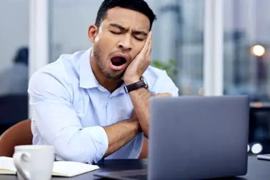 Drowsy adult with heavy eyelids yawning while sitting at a desk