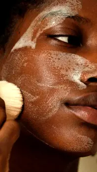 Person scrubbing their face vigorously with a textured exfoliating product, leaving the skin red and irritated.