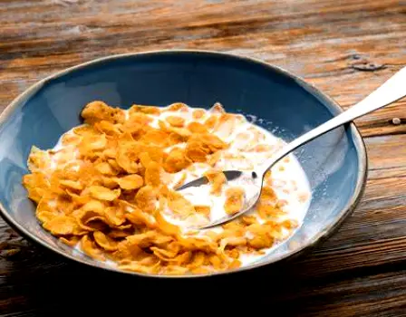 Bowl of fortified breakfast cereal with plant-based milk beside a carton and spoon