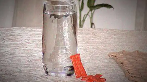 A tall glass of water next to a few pieces of sugarless gum on a table