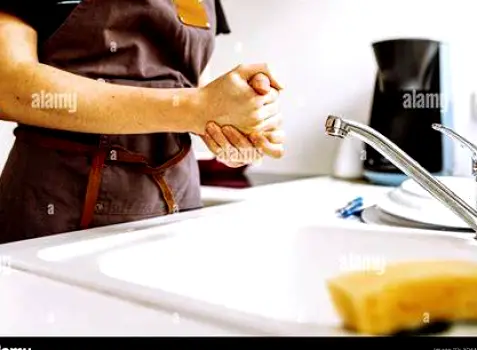 Tube of hand moisturizer standing on a bathroom sink edge above freshly washed hands with dry, cracked knuckles