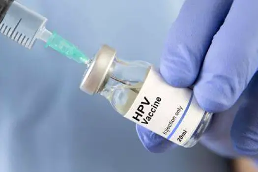 A HPV vaccine vial and syringe prepared on a clinical tray in a medical exam room