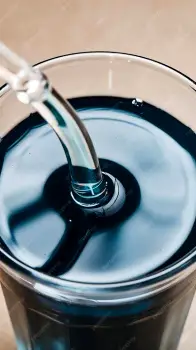 Glass of dark liquid iron supplement with a straw beside a bottle of liquid iron