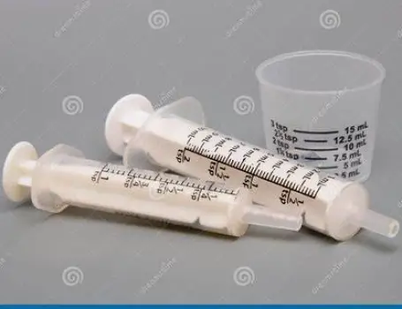 Oral liquid medicine in a dosing cup beside an oral syringe and a plain medicine bottle