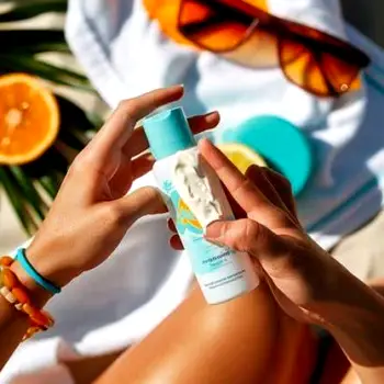 Person applying broad-spectrum sunscreen to their face while standing outdoors in sunlight