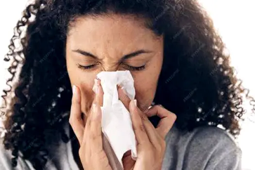 Person holding a tissue over their nose and blowing, with used tissues on a table nearby