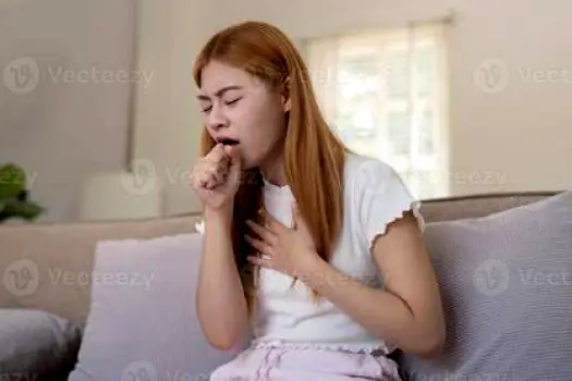Person sitting on a sofa holding a tissue while coughing, illustrating lingering respiratory symptoms