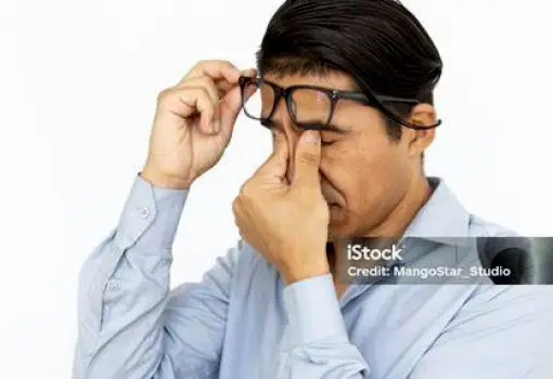 Person looking visibly fatigued and rubbing their eyes while sitting at a desk