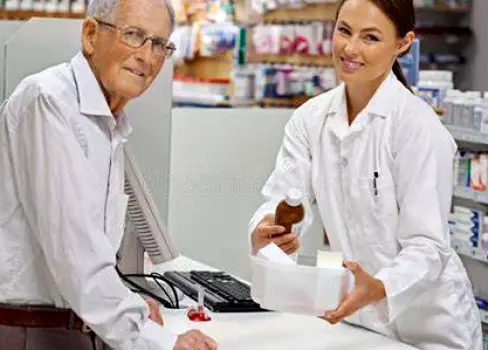 Person holding medicine containers while talking with a pharmacist across a pharmacy counter