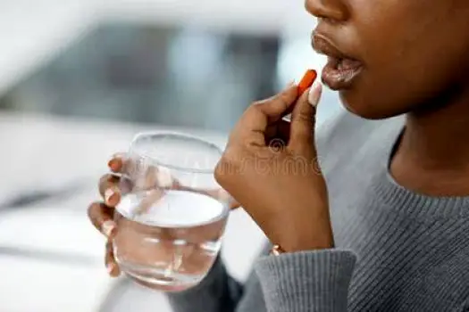 Person sitting upright drinking a glass of water after taking a tablet.