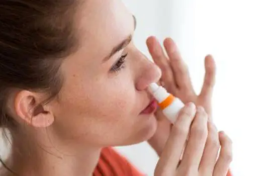 Person holding a saline nasal spray bottle near the nostril