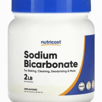 A spoon of white sodium bicarbonate powder next to a glass of water